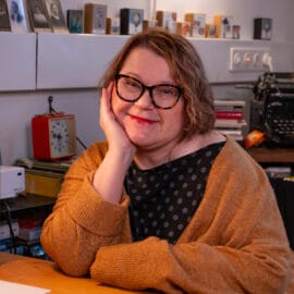 Jaana Lindfors istuu pöydälla ja hymyilee.